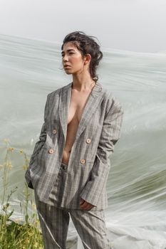 An Asian model poses in a field of yellow flowers for a clothing brand, polyethylene is the main props for a photo shoot. The concept of manufacturing clothing from recycled plastic. A woman in a pantsuit is standing on a plastic bag.