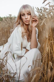 A blonde woman in a long white dress walks in a wheat field. The concept of a wedding and walking in nature.