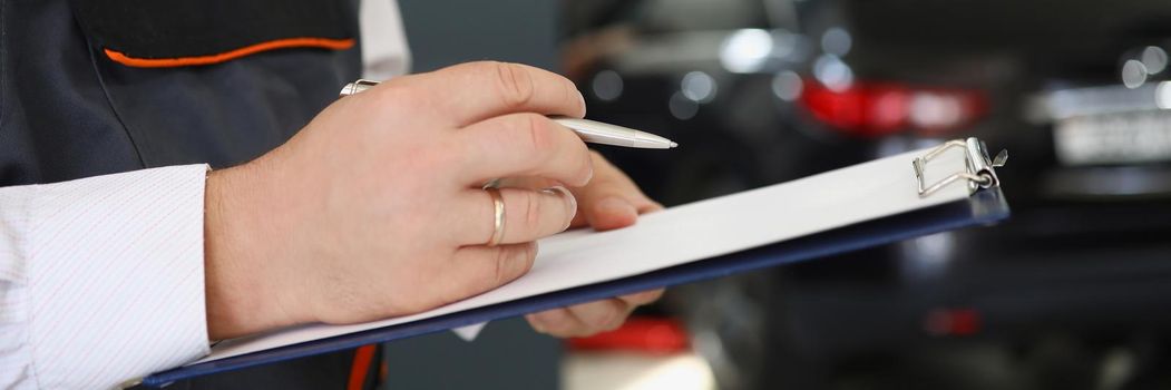 Man repairman standing with clipboard with documents at car repair shop closeup. Auto insurance concept