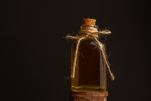 close-up of a glass bottle with cork stopper and raffia rope with rosemary oil on a dark background