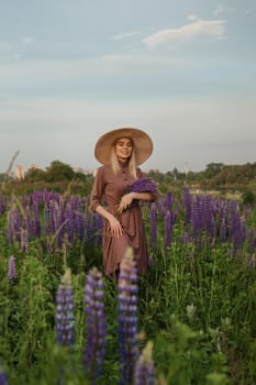 A beautiful woman in a straw hat walks in a field with purple flowers. A walk in nature in the lupin field.