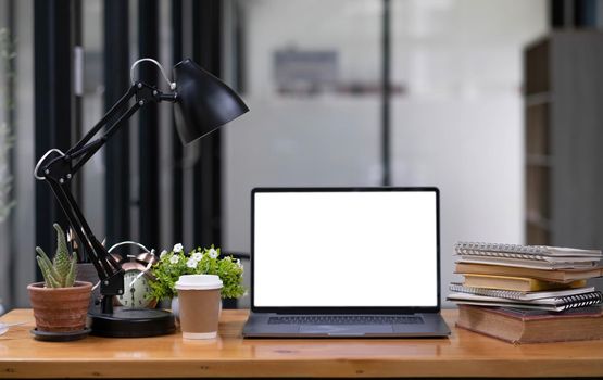 Front view computer laptop with empty screen, coffee cup, pencil holder, notebook and house plant on wooden table..