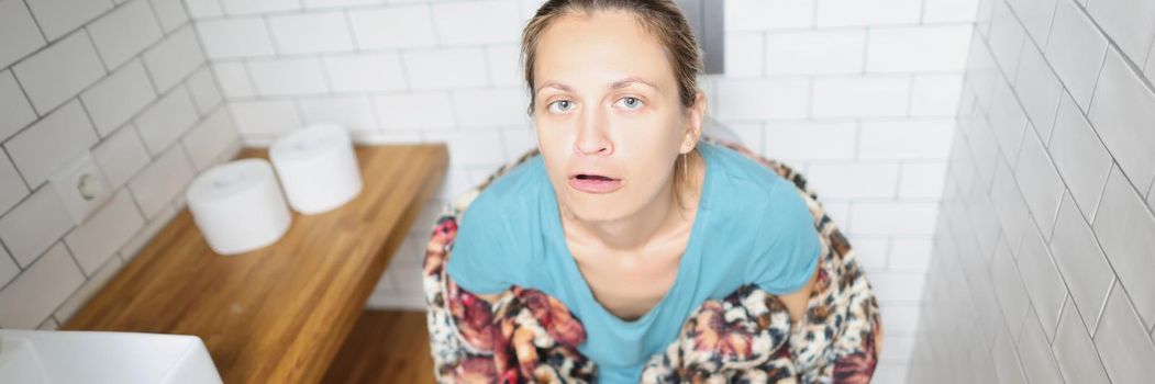 Young woman sitting on toilet and grimacing. Diarrhea treatment concept