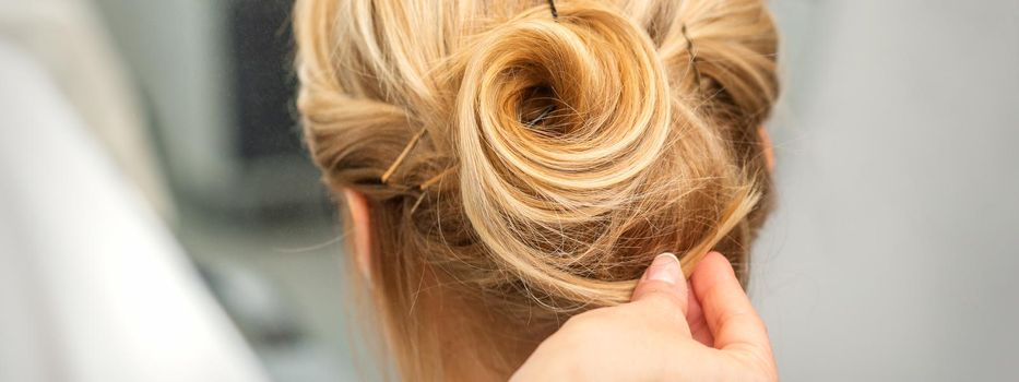 Close up of female hairdresser styling blonde hair of a young woman in a beauty salon