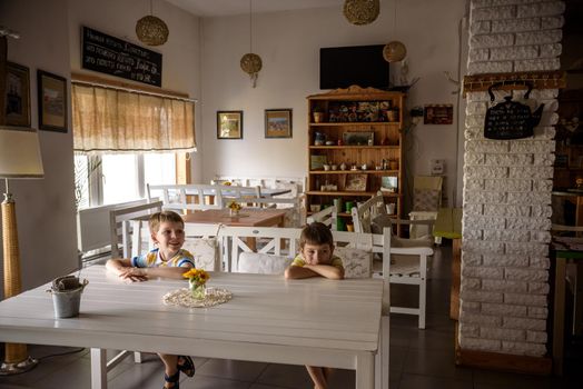 Modern cafe interior style, eco environmental with plant on wall, coffee shop. Two children sitting on bench near table waiting for tasty meal.