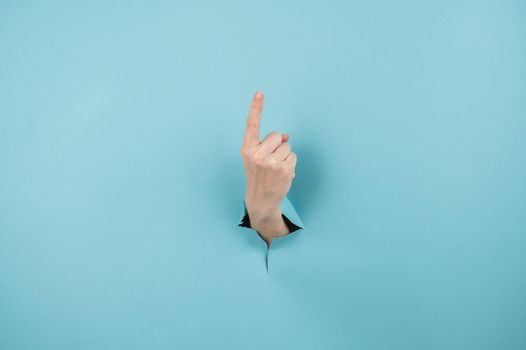 A woman's hand sticking out of a hole from a blue background shows her index finger up