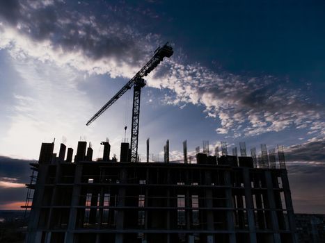 Tower crane and building construction site silhouette at sunrise. The construction crane and the building against the blue sky. download photo