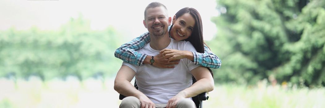 Woman hugging man in wheelchair in park portrait. Close relationship with disabled people concept