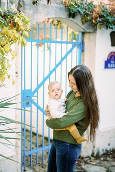 Mom with a baby in her arms stands in front of a metal gate. High quality photo