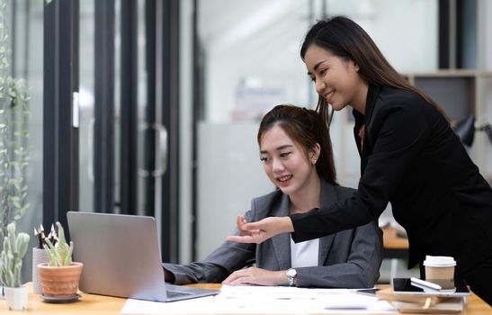 Two young Asian business woman talk, consult, discuss working with new startup project idea presentation analyze plan marketing and investment in the office..