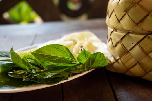 Bamboo wicker sticky rice basket called "Kratip" in the northeastern province, Thailand served with a vegetable side dish on the wooden table.