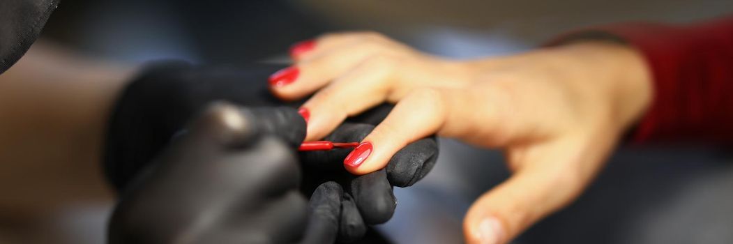 Manicurist painting woman nails with red varnish closeup. Beauty industry concept