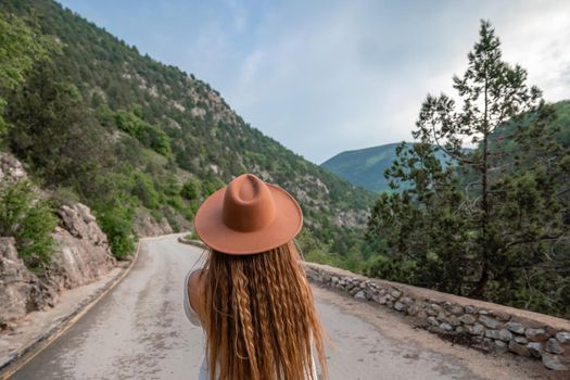 Female traveler in brown hat and white dress looking at amazing mountains and forest, wanderlust travel concept, atmospheric epic moment.