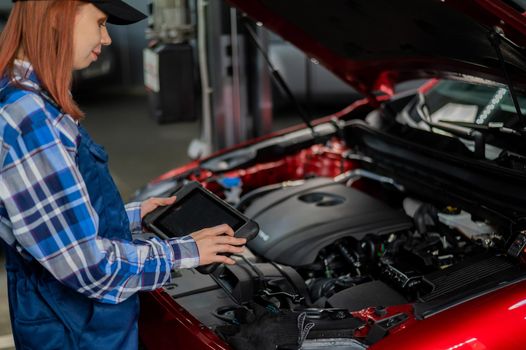 Caucasian female auto mechanic uses a special computer to diagnose faults