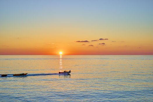 Sunset over the sea with a sailing boat in the distance. Beautiful seascape from the shore.