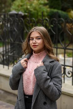 young beautiful girl posing on the street. Dressed in a stylish gray coat, knitted pink sweater and skirt.