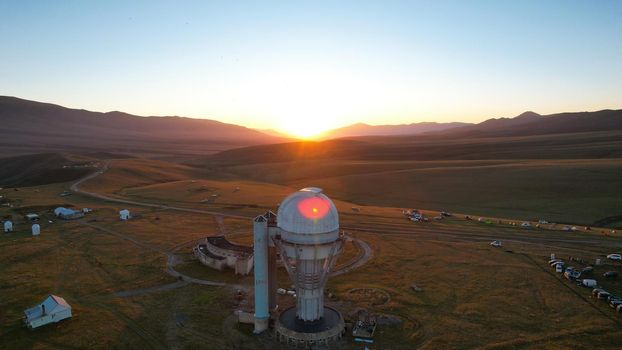 Bright dawn over the Assy-Turgen Observatory in the mountains. Aerial view from the drone of the camp of tents, cars and waking tourists. There is an old abandoned building. Kazakhstan, Almaty