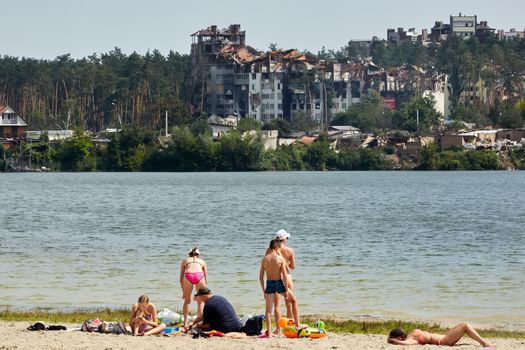 Irpin, Kyiv region, Ukraine - 25 August, 2022: Citi after the Russian occupation. People are having rest near lake opposite destroyed houses