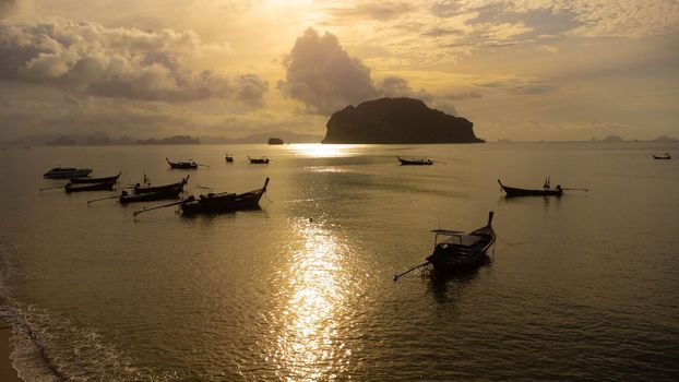 Aerial view from drones of fishing boats in the shore during sunset. Top view of many Thai traditional longtail fishing boats in the tropical sea.