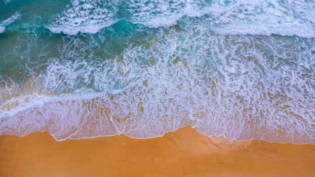 Beautiful sea waves and white sand beach in the tropical island. Soft waves of blue ocean on sandy beach background from top view from drones. Concept of relaxation and travel on vacation.