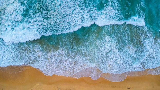 Beautiful sea waves and white sand beach in the tropical island. Soft waves of blue ocean on sandy beach background from top view from drones. Concept of relaxation and travel on vacation.