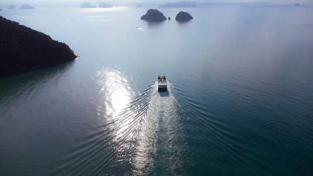 An aerial view of a yacht sailing in the Andaman Sea at sunset. Top view of a sailboat on the sea surface and the beautiful nature of the islands in the tropical sea.