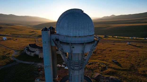 Bright dawn over the Assy-Turgen Observatory in the mountains. Aerial view from the drone of the camp of tents, cars and waking tourists. There is an old abandoned building. Kazakhstan, Almaty