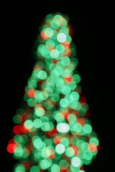 Blurred background, bokeh with colorful lights, holiday lighting. Abstract blur. Beautiful small Christmas tree.