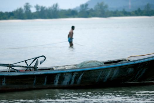 Thai small fishing boat moored on the beach with fishermen preparing to go fishing in the morning in the background. Life in the traditional Thai countryside.