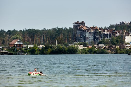 Irpin, Kyiv region, Ukraine - 25 August, 2022: Citi after the Russian occupation. People are having rest near lake opposite destroyed houses