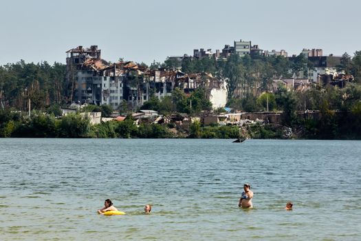 Irpin, Kyiv region, Ukraine - 25 August, 2022: Citi after the Russian occupation. People are having rest near lake opposite destroyed houses