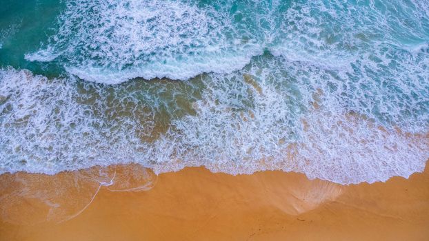 Beautiful sea waves and white sand beach in the tropical island. Soft waves of blue ocean on sandy beach background from top view from drones. Concept of relaxation and travel on vacation.