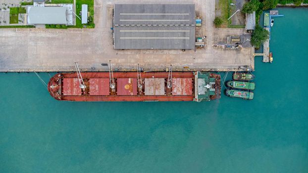 Aerial view from drone of commercial ship with cranes while unloading containers to large commercial ship in the wharf. Transportation and travel background, beautiful sea in summer.