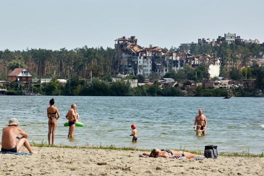 Irpin, Kyiv region, Ukraine - 25 August, 2022: Citi after the Russian occupation. People are having rest near lake opposite destroyed houses
