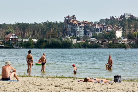 Irpin, Kyiv region, Ukraine - 25 August, 2022: Citi after the Russian occupation. People are having rest near lake opposite destroyed houses