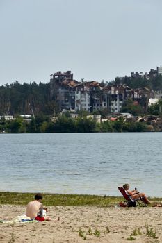 Irpin, Kyiv region, Ukraine - 25 August, 2022: Citi after the Russian occupation. People are having rest near lake opposite destroyed houses