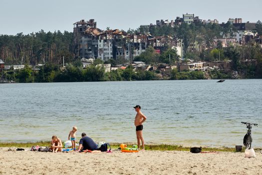 Irpin, Kyiv region, Ukraine - 25 August, 2022: Citi after the Russian occupation. People are having rest near lake opposite destroyed houses