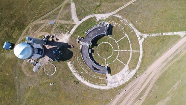 An abandoned building with a beautiful pattern of paths. The Assy-Turgen Observatory. The paths are laid out in the form of a telescope. Green grass grows, and purple bushes grow on the roof. Drone