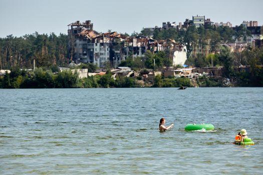 Irpin, Kyiv region, Ukraine - 25 August, 2022: Citi after the Russian occupation. People are having rest near lake opposite destroyed houses