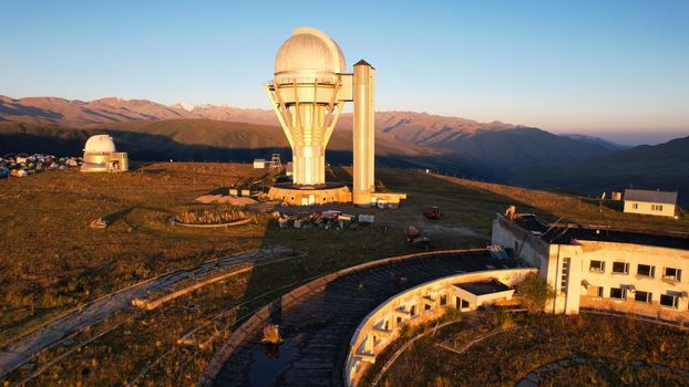 Bright dawn over the Assy-Turgen Observatory in the mountains. Aerial view from the drone of the camp of tents, cars and waking tourists. There is an old abandoned building. Kazakhstan, Almaty