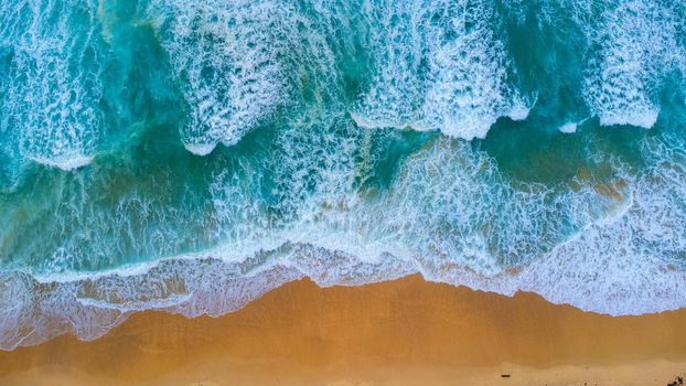 Beautiful sea waves and white sand beach in the tropical island. Soft waves of blue ocean on sandy beach background from top view from drones. Concept of relaxation and travel on vacation.