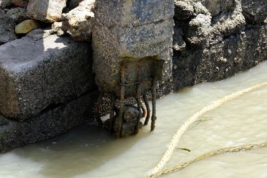 Old rusted metal pier or wharf where small fishing boats are moored. The base of an old concrete pier in tropical sea. The concept of mooring and water transportation