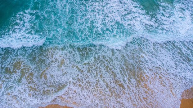 Beautiful sea waves and white sand beach in the tropical island. Soft waves of blue ocean on sandy beach background from top view from drones. Concept of relaxation and travel on vacation.