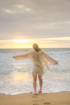 Portrait of a beautiful Asian woman smiling relaxing on the beach. A young woman strolling along the sea looking at the big waves and strong winds. Concept of relaxation and travel on vacation.