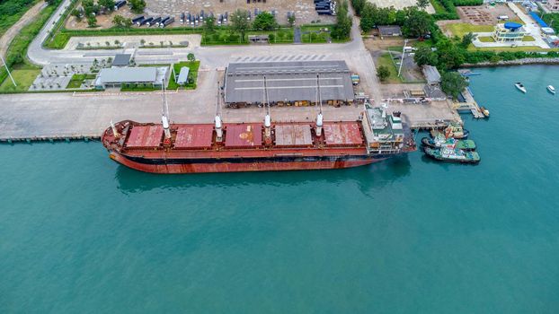 Aerial view from drone of commercial ship with cranes while unloading containers to large commercial ship in the wharf. Transportation and travel background, beautiful sea in summer.