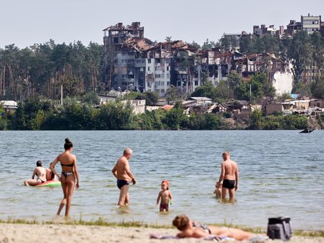 Irpin, Kyiv region, Ukraine - 25 August, 2022: Citi after the Russian occupation. People are having rest near lake opposite destroyed houses