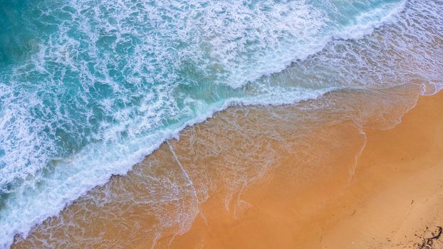 Beautiful sea waves and white sand beach in the tropical island. Soft waves of blue ocean on sandy beach background from top view from drones. Concept of relaxation and travel on vacation.