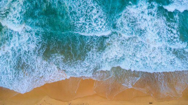 Beautiful sea waves and white sand beach in the tropical island. Soft waves of blue ocean on sandy beach background from top view from drones. Concept of relaxation and travel on vacation.