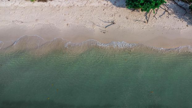 Beautiful sea waves and white sand beach in the tropical island. Soft waves of blue ocean on sandy beach background from top view from drones. Concept of relaxation and travel on vacation.