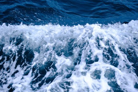 Waves beside the boat are sailing in the sea in the summer. Background of blue ocean waves and white foam bubbles.